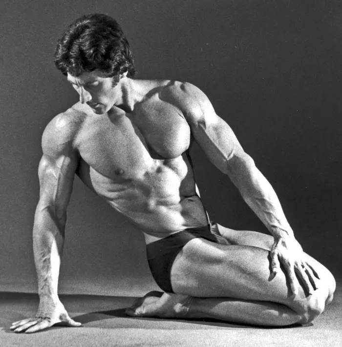 A dramatic side-lit studio portrait catches Zane in an unusual kneeling pose, pure artistic composition in black and white.