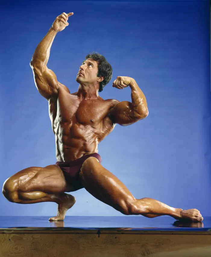A sharp, dynamic bicep-flex pose against a saturated blue studio backdrop from a rare editorial shoot.