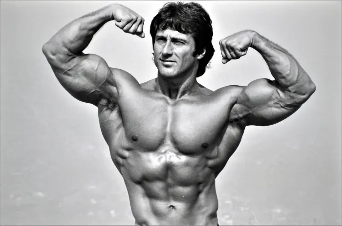 A tight-crop back double-biceps shot against a glowing sky, showcasing the back that defined his physique.