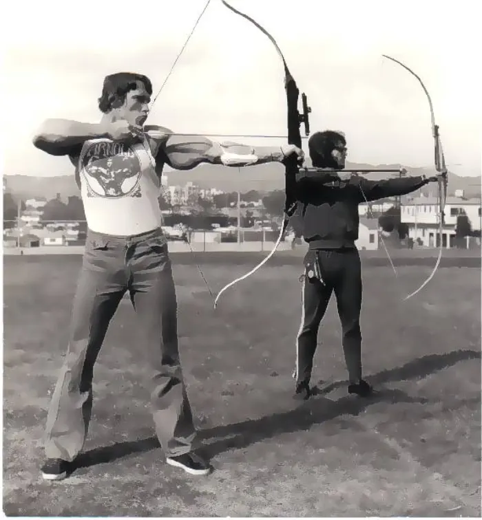 An informal candid of Zane practicing archery alongside a recognizable Arnold Schwarzenegger.