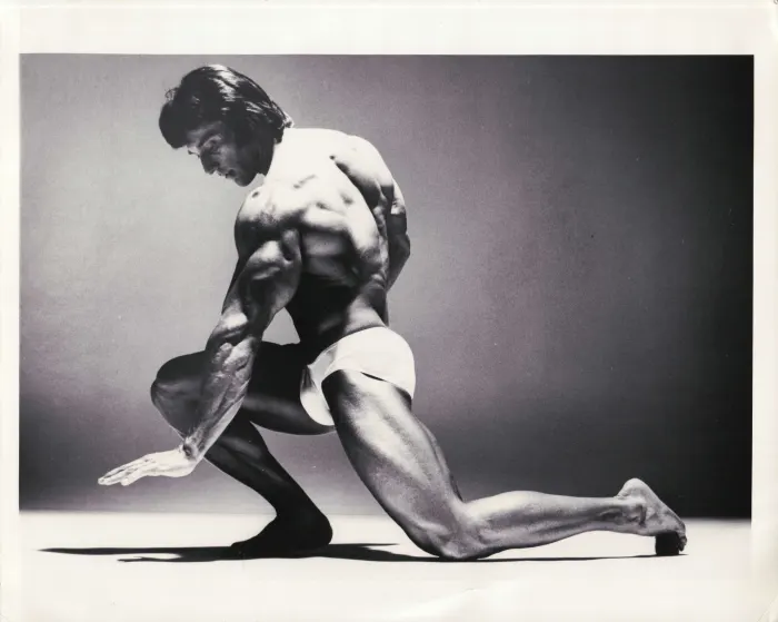 A beautifully lit Richard Avedon studio shot, a dramatic kneeling lunge with extended arm.