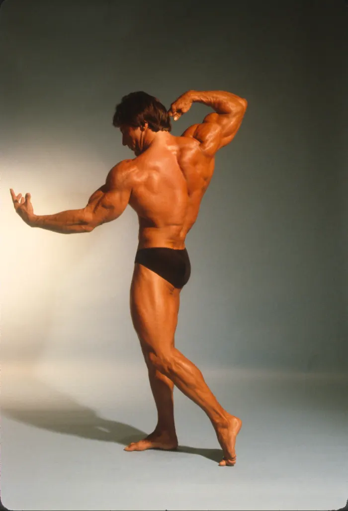 A dynamic back-triceps transition pose under dramatic gradient studio lighting.
