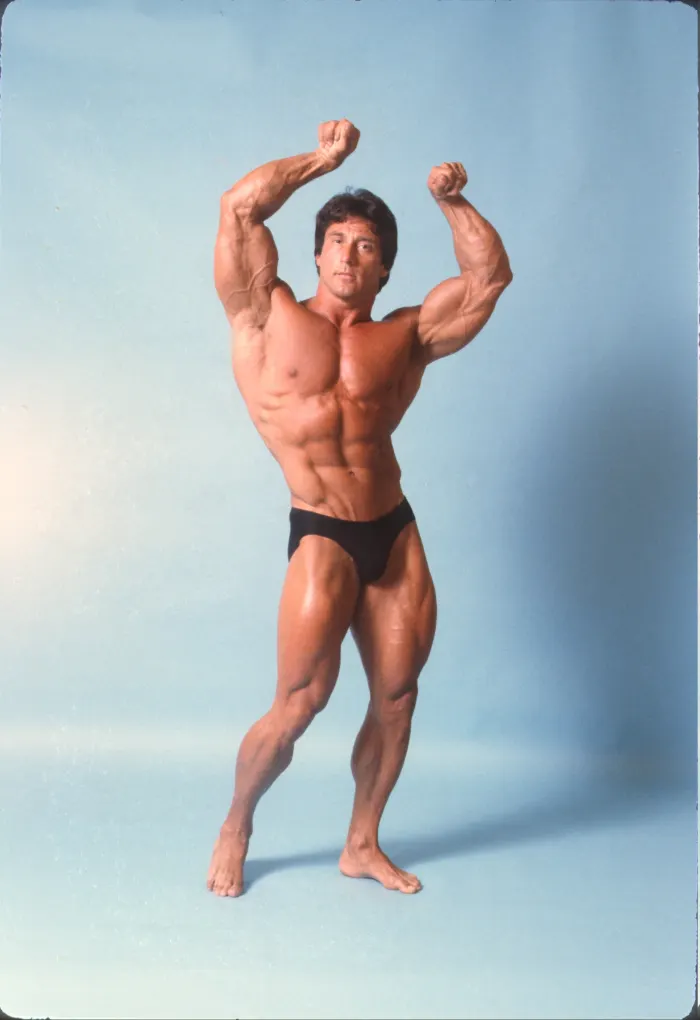 A clean studio backdrop and crisp lighting frame the classic double-biceps pose.