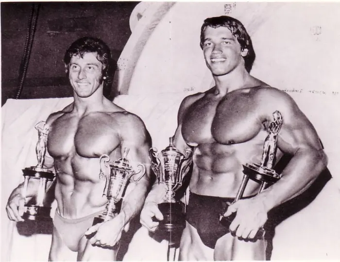 A rare backstage photo of a young Frank Zane and Arnold Schwarzenegger together, holding trophies.