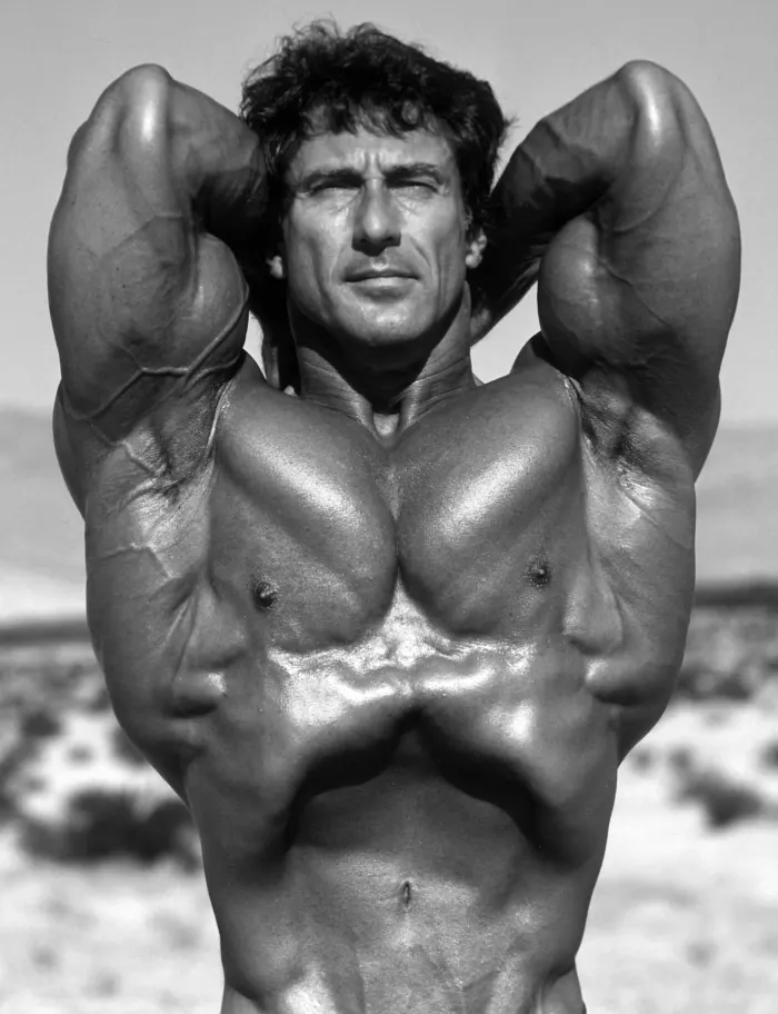 A rare vacuum pose on the beach, arms raised, abdomen pulled in, crisp black-and-white contrast.