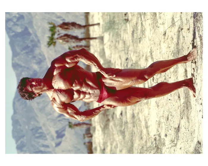 A high-resolution color portrait in red trunks against dramatic sand dunes.